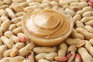 Bowl of peanut butter surrounded by peanuts in shell.