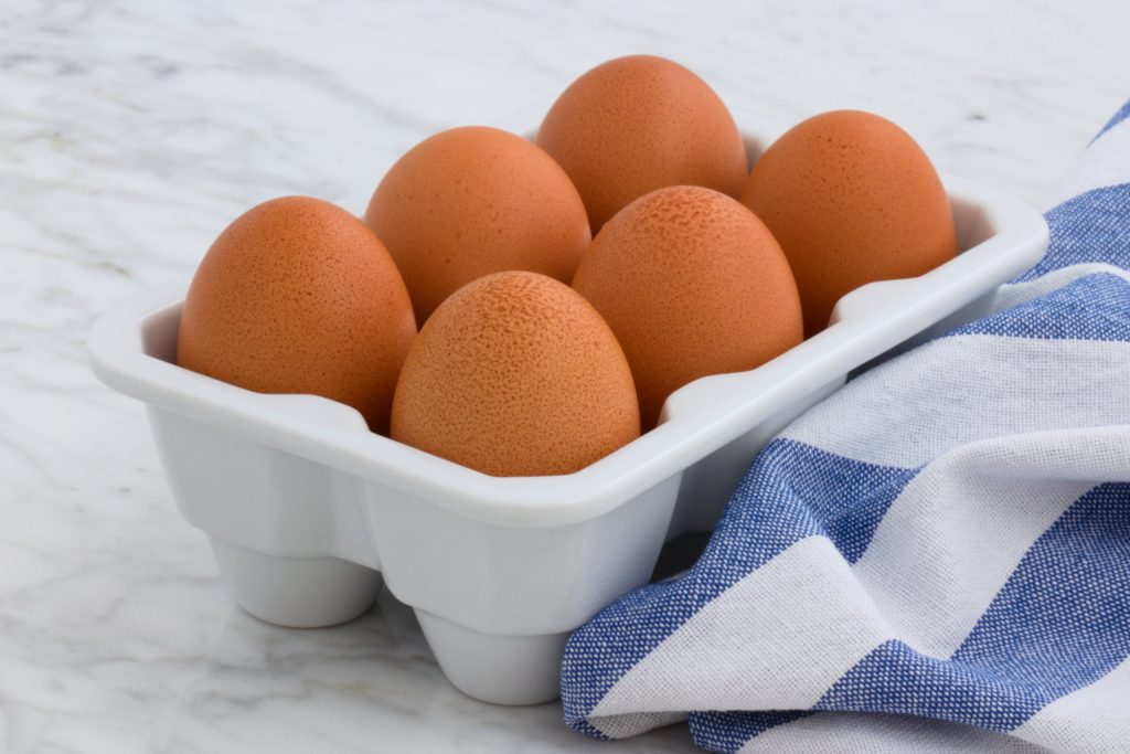 Eggs in 6-pack carton on counter with blue and white cloth.