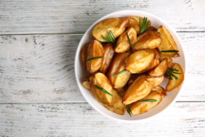 Baked potato wedges in white bowl on light grey wooden table.