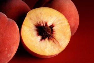 Peaches with one cut in half on red background.