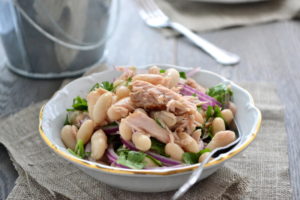 Tuna with white beans, red onion and greens in bowl.