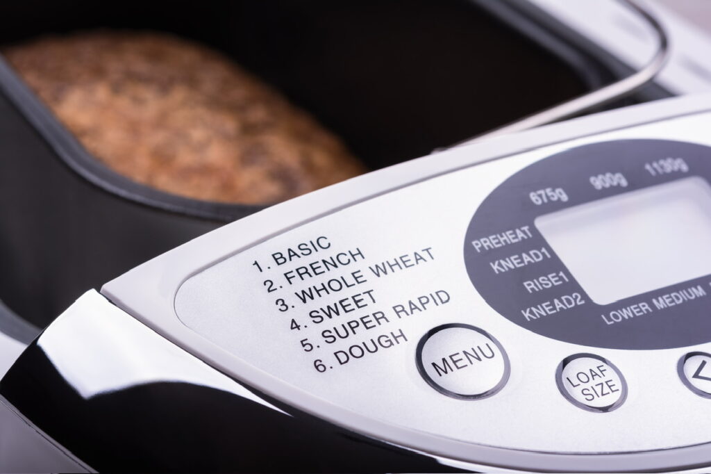 Bread machine showing close-up of digital display that includes whole wheat setting.